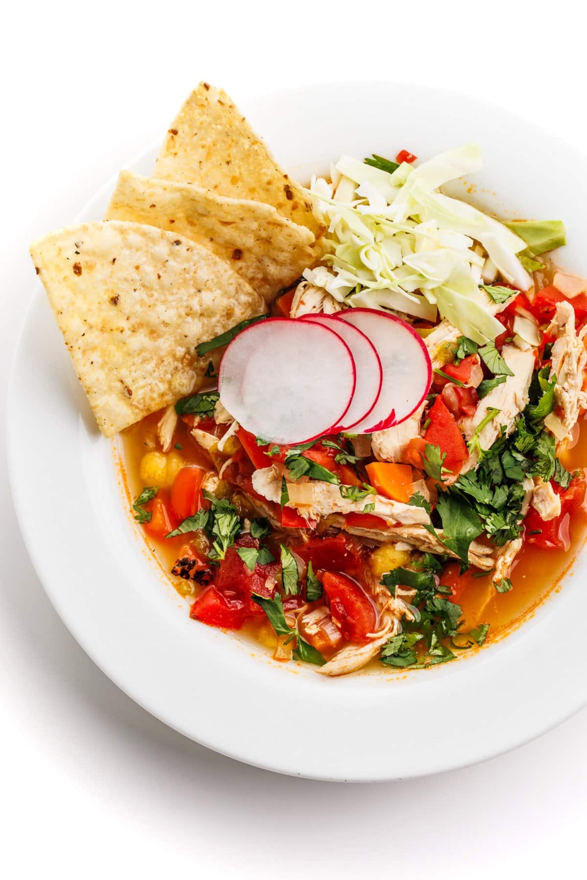 Mexican chicken pozole soup in a white bowl, garnished with radishes and tortilla chips.
