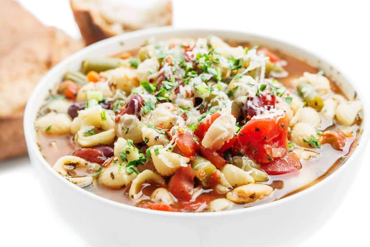 Minestrone soup in a bowl with crust bread in the background.
