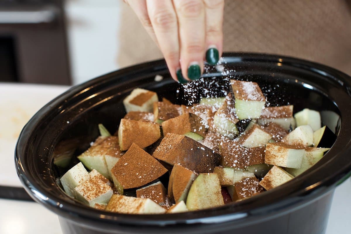 Seasoning eggplant with Lebanese spice blend in slow cooker bowl.