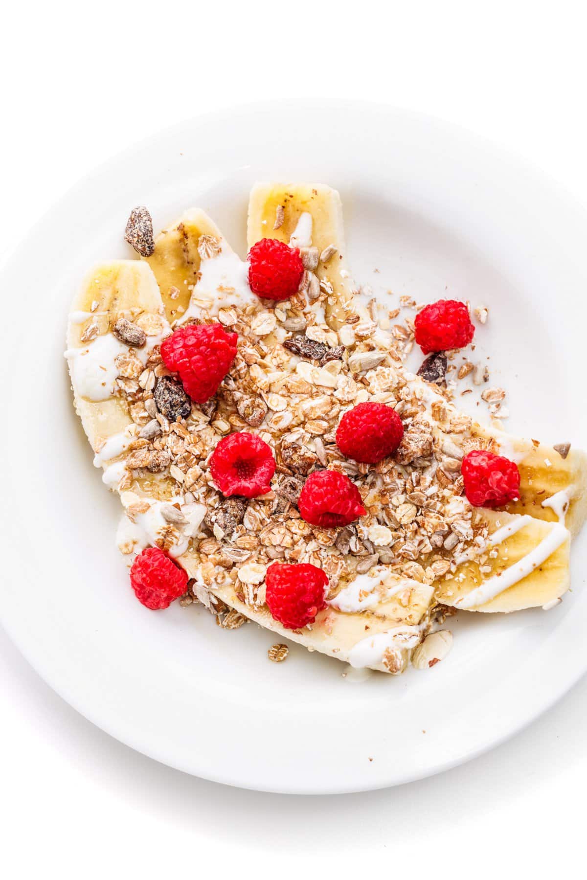 Yogurt banana splits with muesli and raspberries on a white plate.