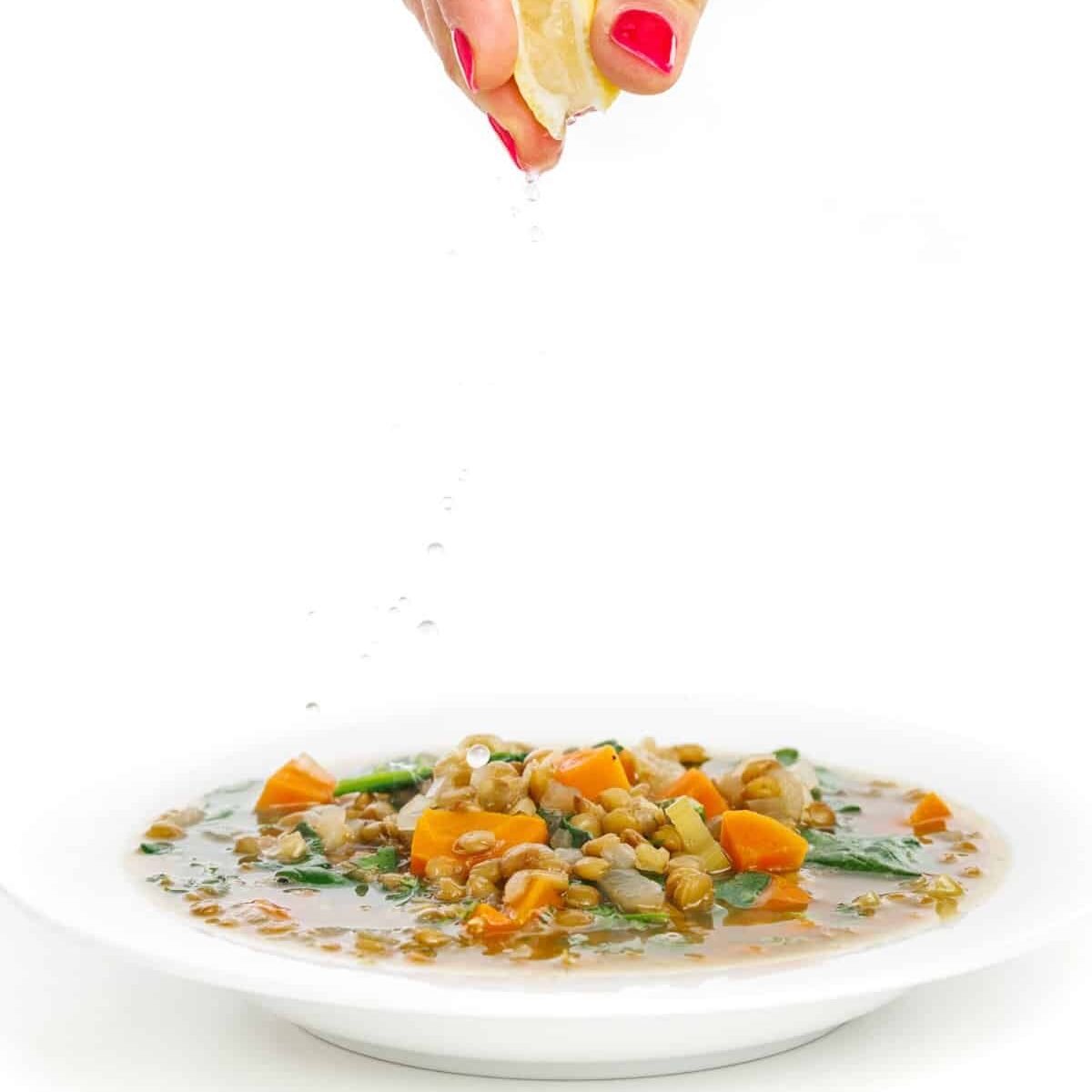 Garnishing lemony lentil soup with spinach with fresh lemon juice.