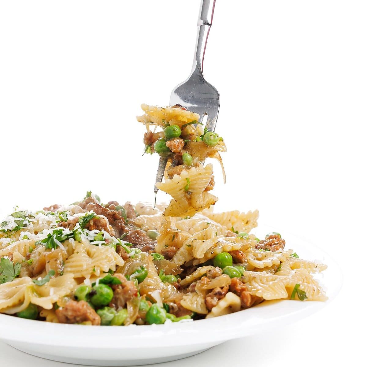 Forkful of sausage pesto pasta with caramelized onions and peas.