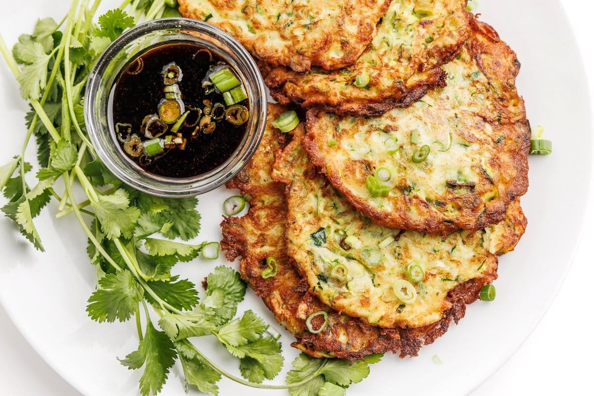 Zucchini scallion pancakes on a plate with sauce and parsley.