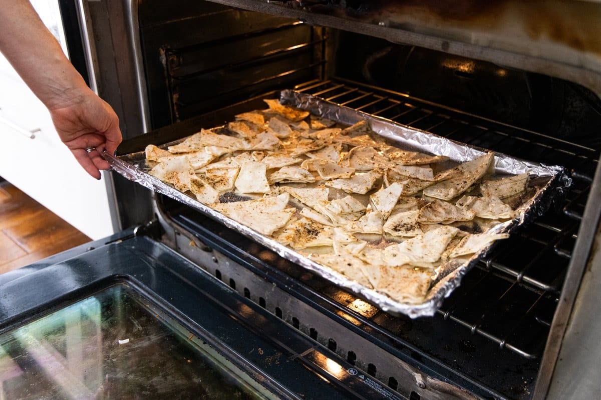 Putting pita triangles on a foil lined baking tray into an oven.
