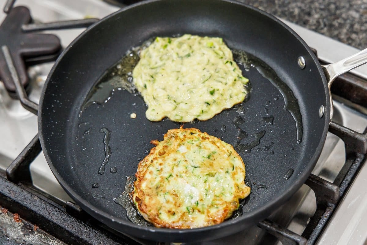 Cooking zucchini scallion pancakes in oil in a skillet.