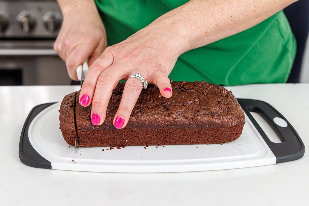 Slicing baked chocolate zucchini carrot bread on a cutting board.