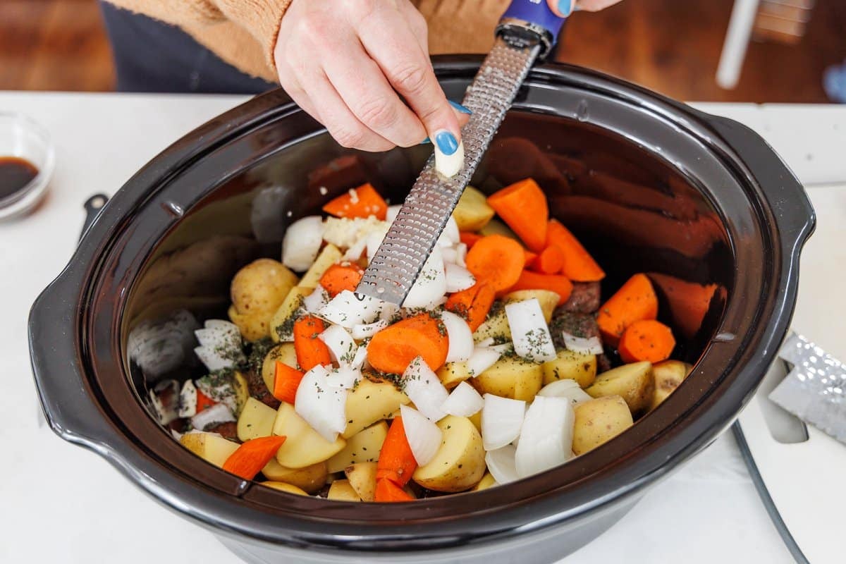 Grating garlic cloves into slow cooker bowl with veggies.