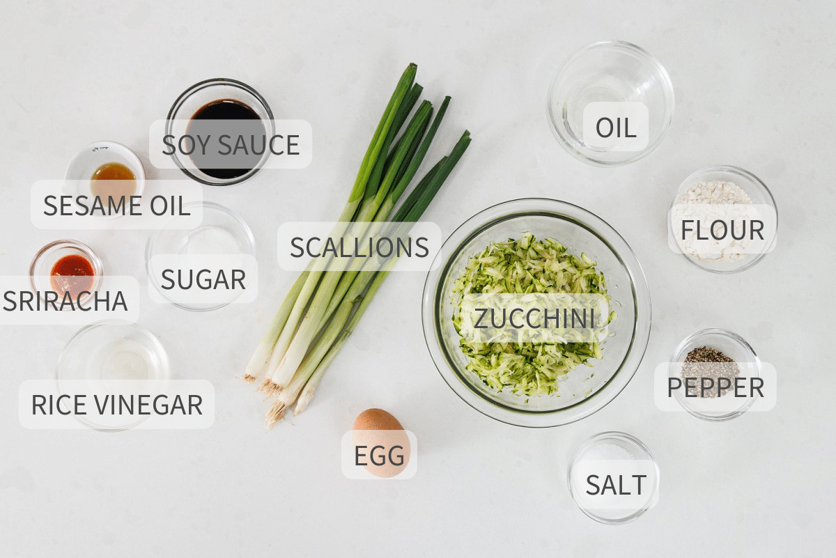 Labeled ingredients for zucchini scallion pancakes on a white background.