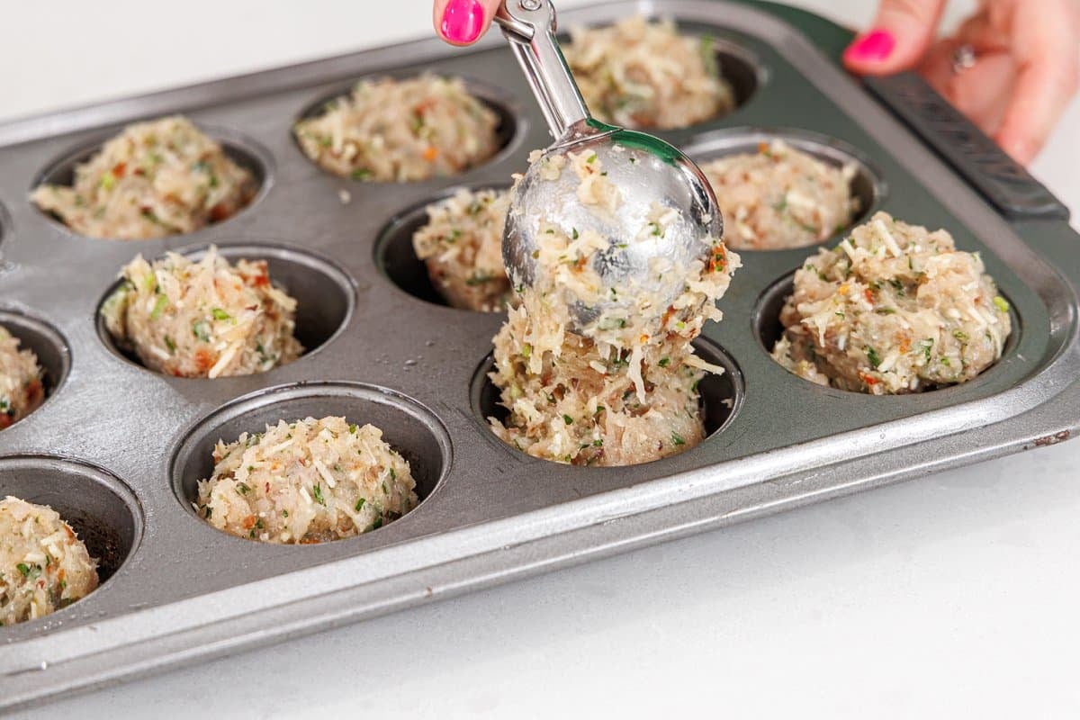 Scooping meatloaf mix into muffin tin.