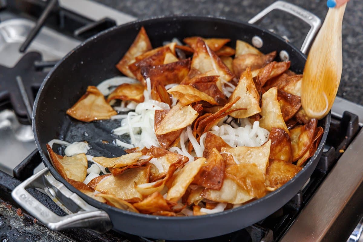 Adding fresh made tortilla chips back to pan with onions.