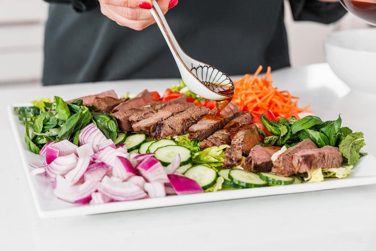 Drizzling dressing over beef salad.