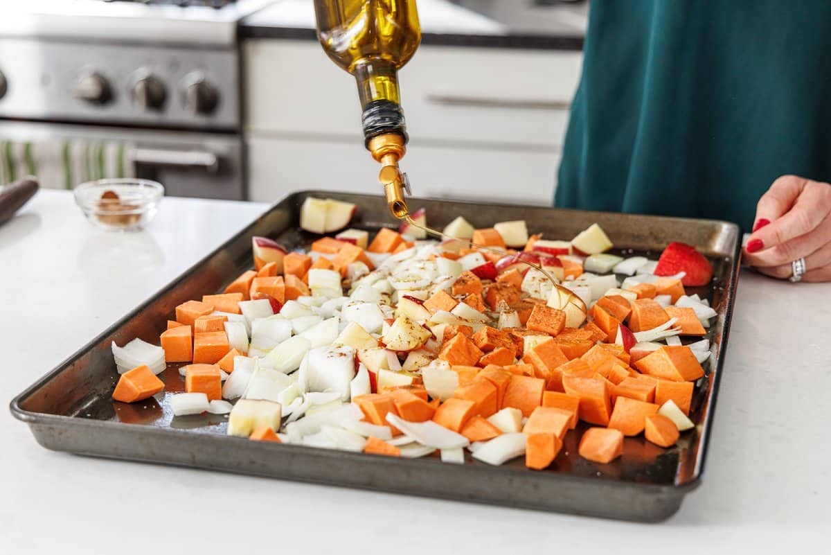 Drizzling olive oil over diced veggies on sheet pan.