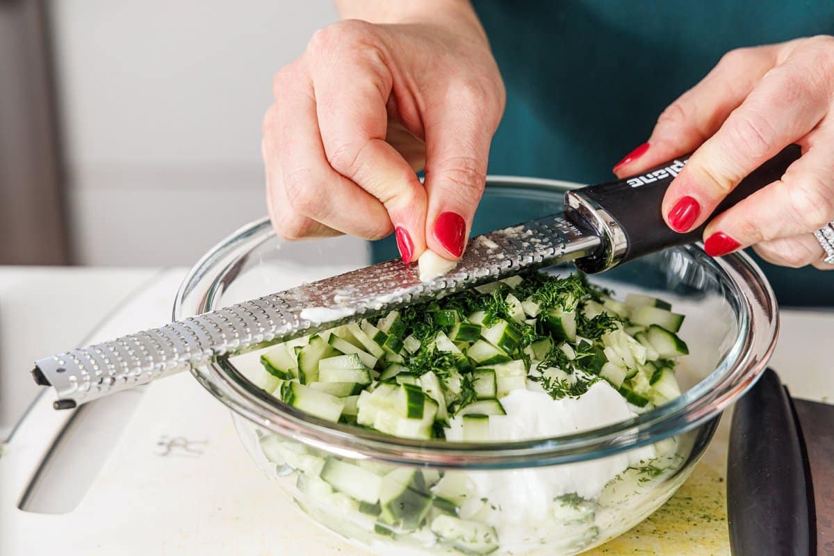 Grating garlic with a microplane into a bowl with yogurt and cucumber.