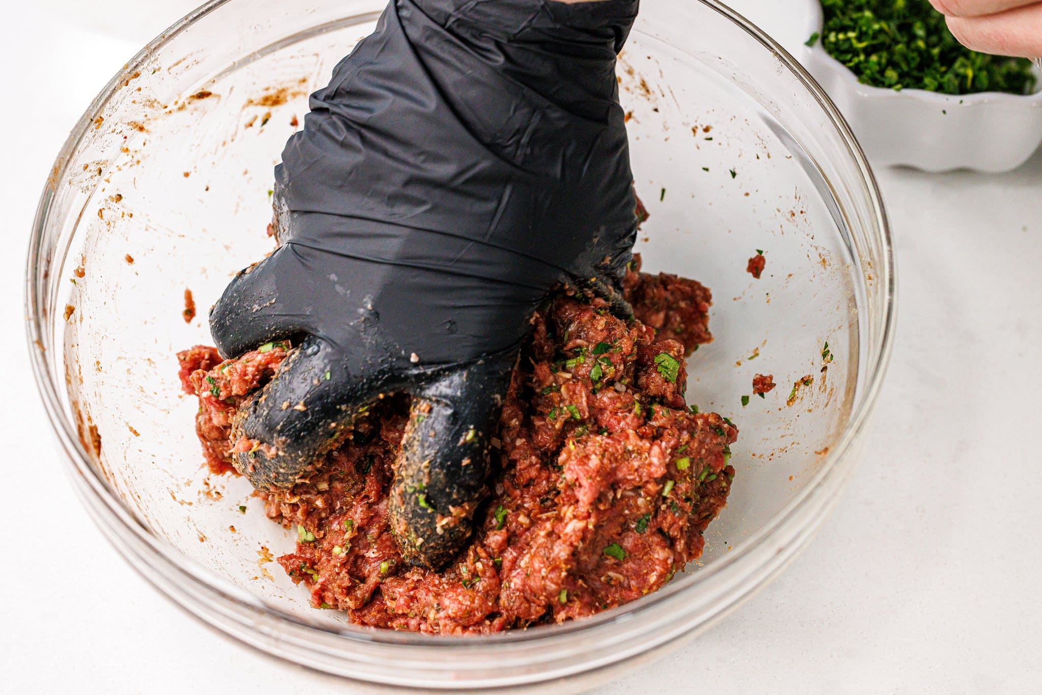 Using a gloved hand to mix meat and seasonings for meatballs.