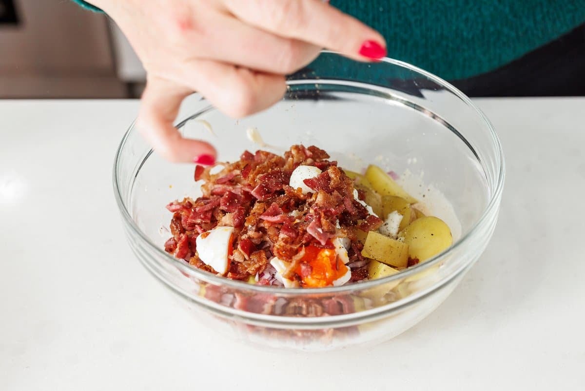 Adding bacon crumbles to potato salad ingredients.