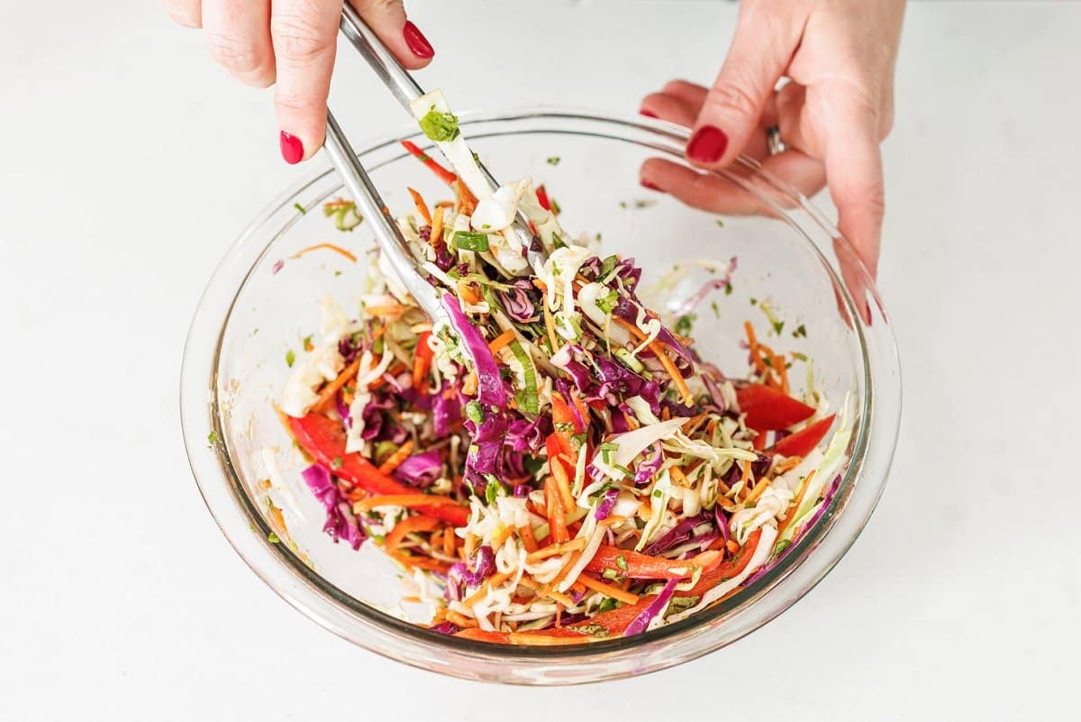 Tossing slaw in vinaigrette with tongs.