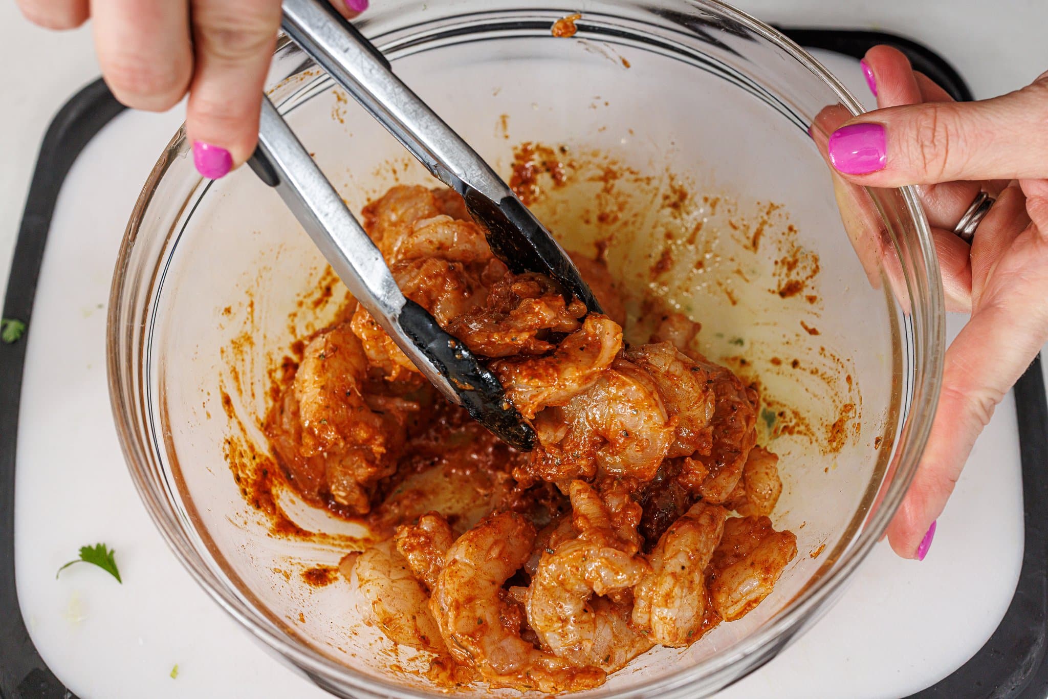 Tossing shrimp in marinade in glass bowl.