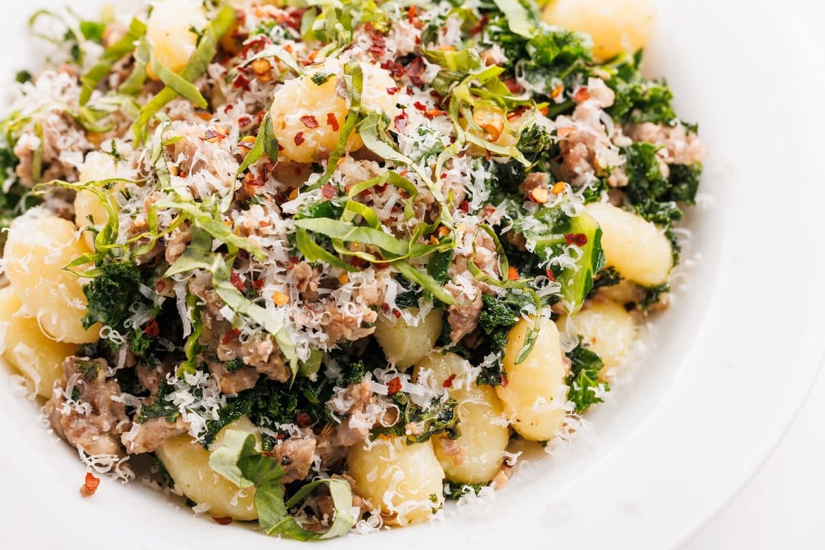 Sausage and kale gnocchi pasta in white bowl.