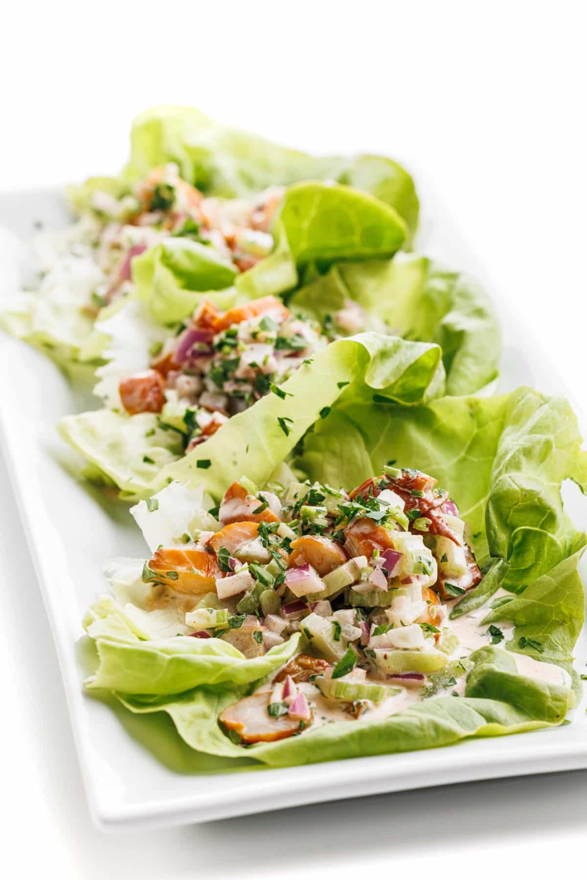 Shrimp salad lettuce cups in a row on a white platter.