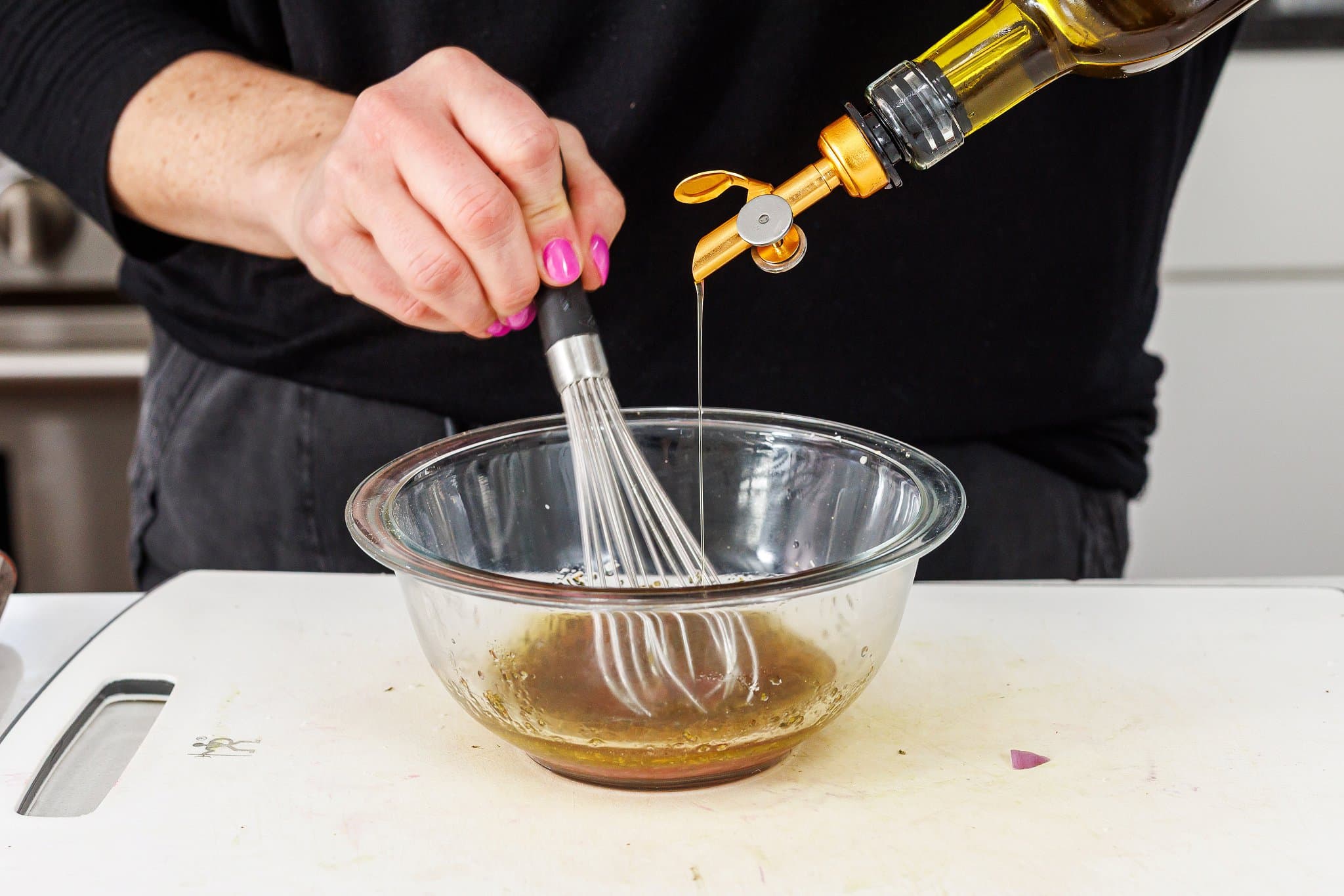 Drizzling olive oil into a bowl and whisking into dressing.