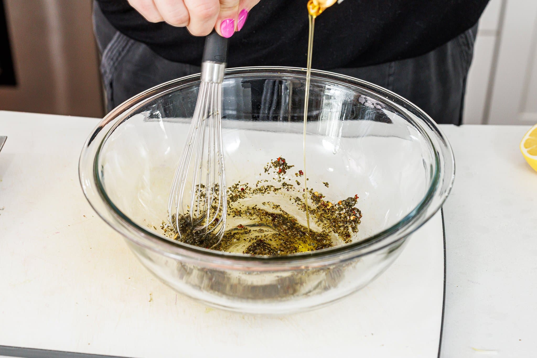 Adding olive oil to oregano and garlic in a bowl.