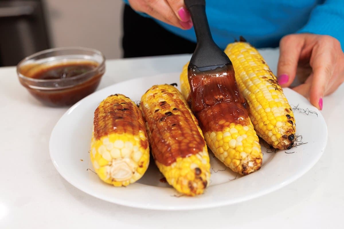 Brushing grilled corn with bbq sauce.