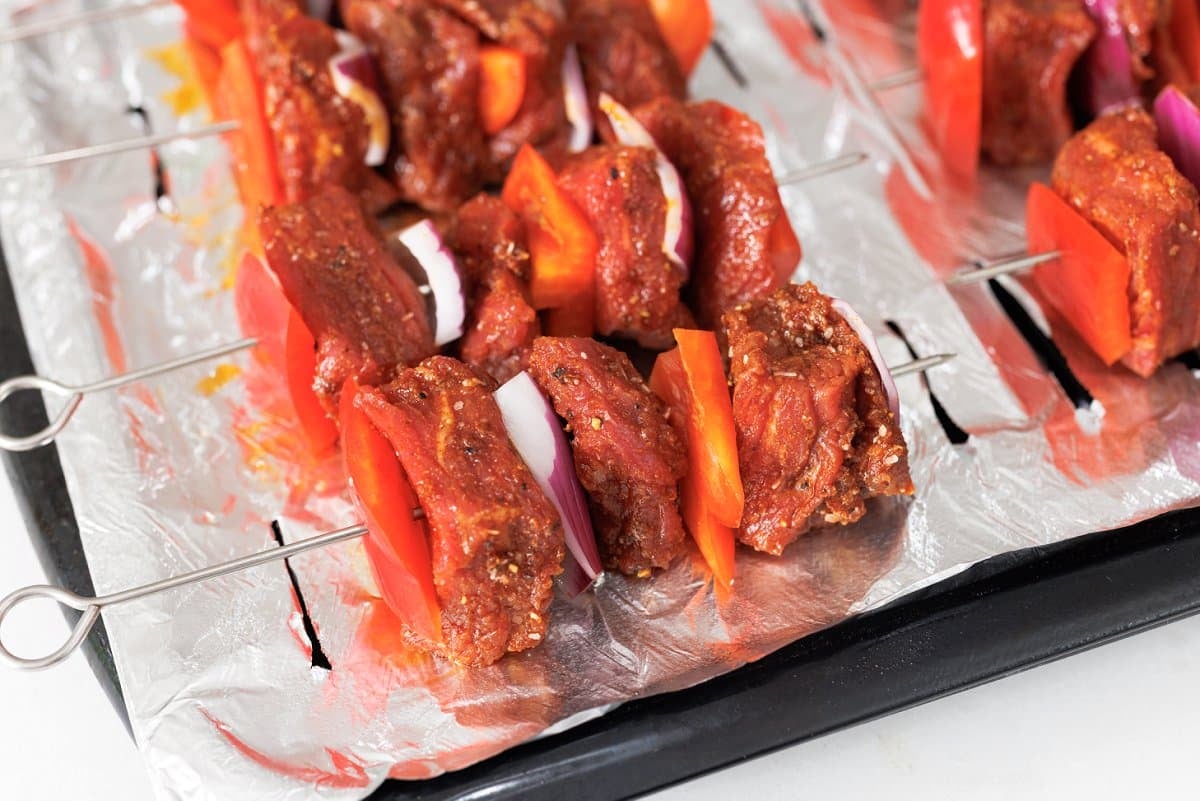 Steak skewers laid out on a baking sheet.