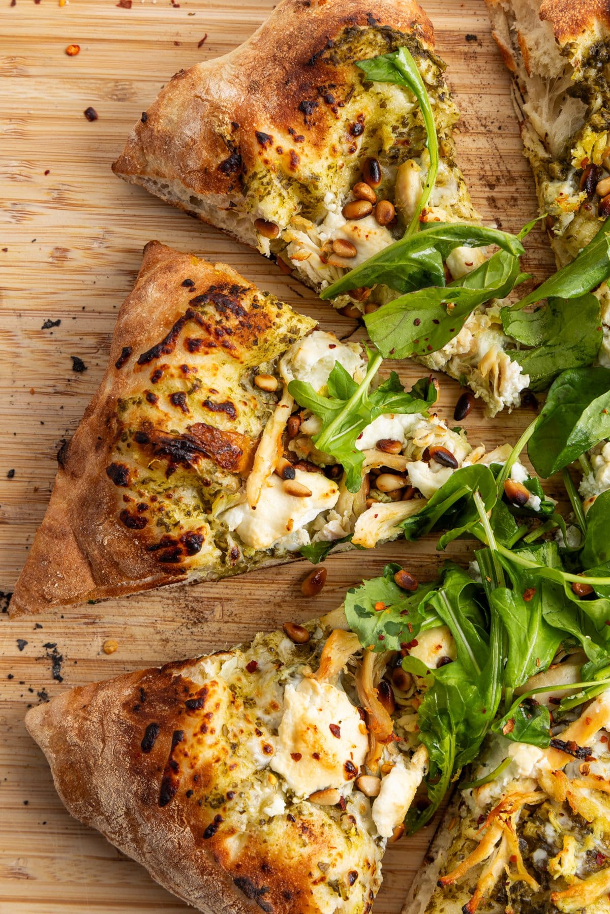 Slices of pesto chicken pizza with goat cheese and toasted pine nuts.