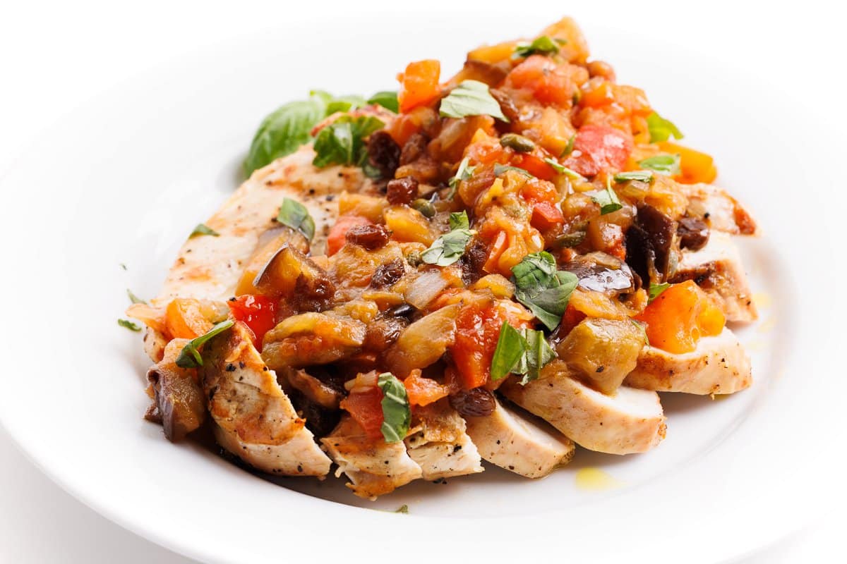 Sliced grilled chicken with eggplant caponata on top in a white dish.