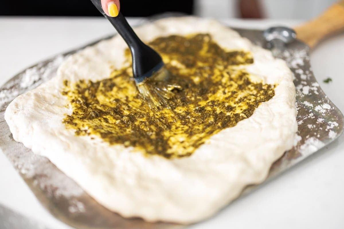 Brushing pesto on raw pizza dough.