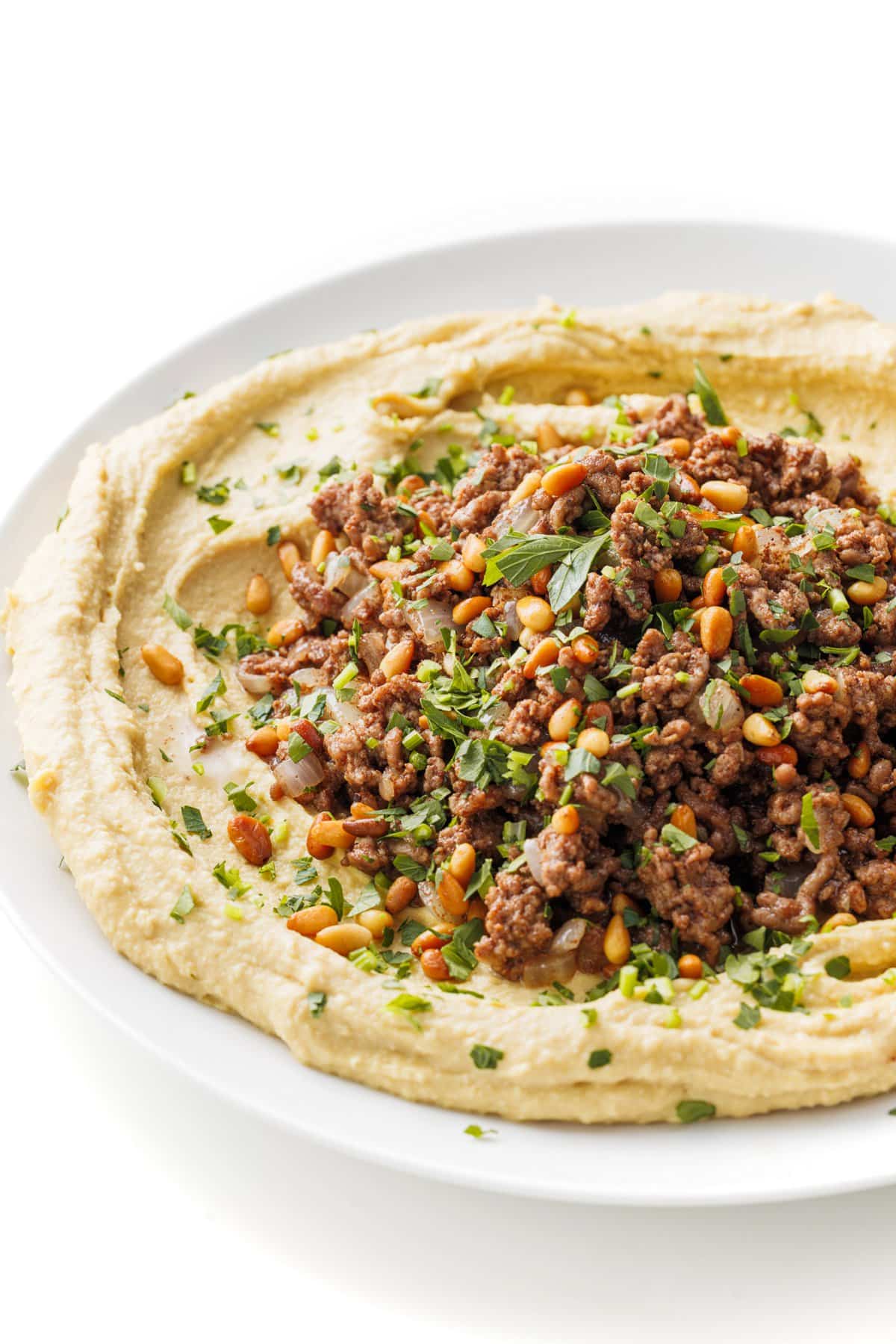 Ground lamb and toasted pine nuts on top of hummus spread on a plate.