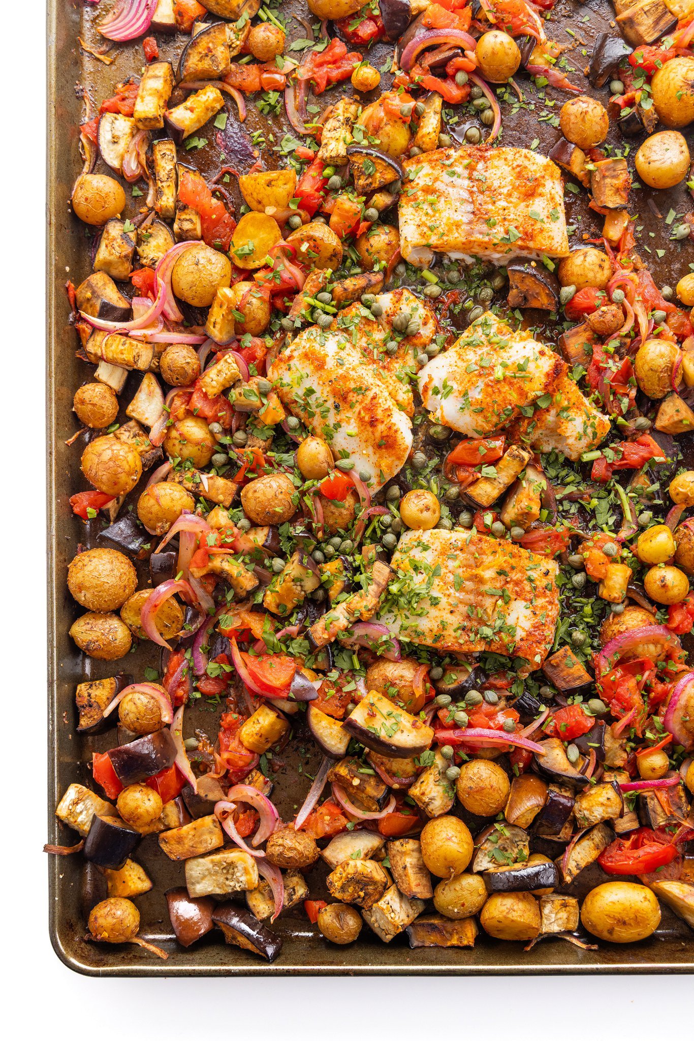 Mediterranean Baked White Fish with Potatoes, Eggplant, and Tomatoes on a sheet pan.