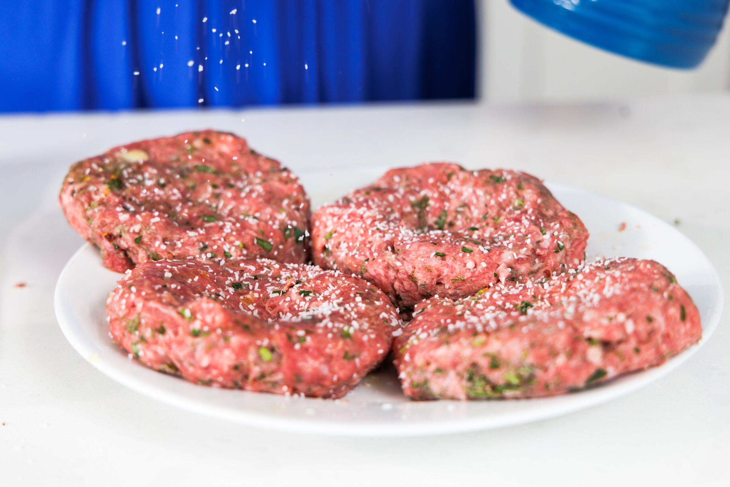 Seasoning ground lamb patties with salt.
