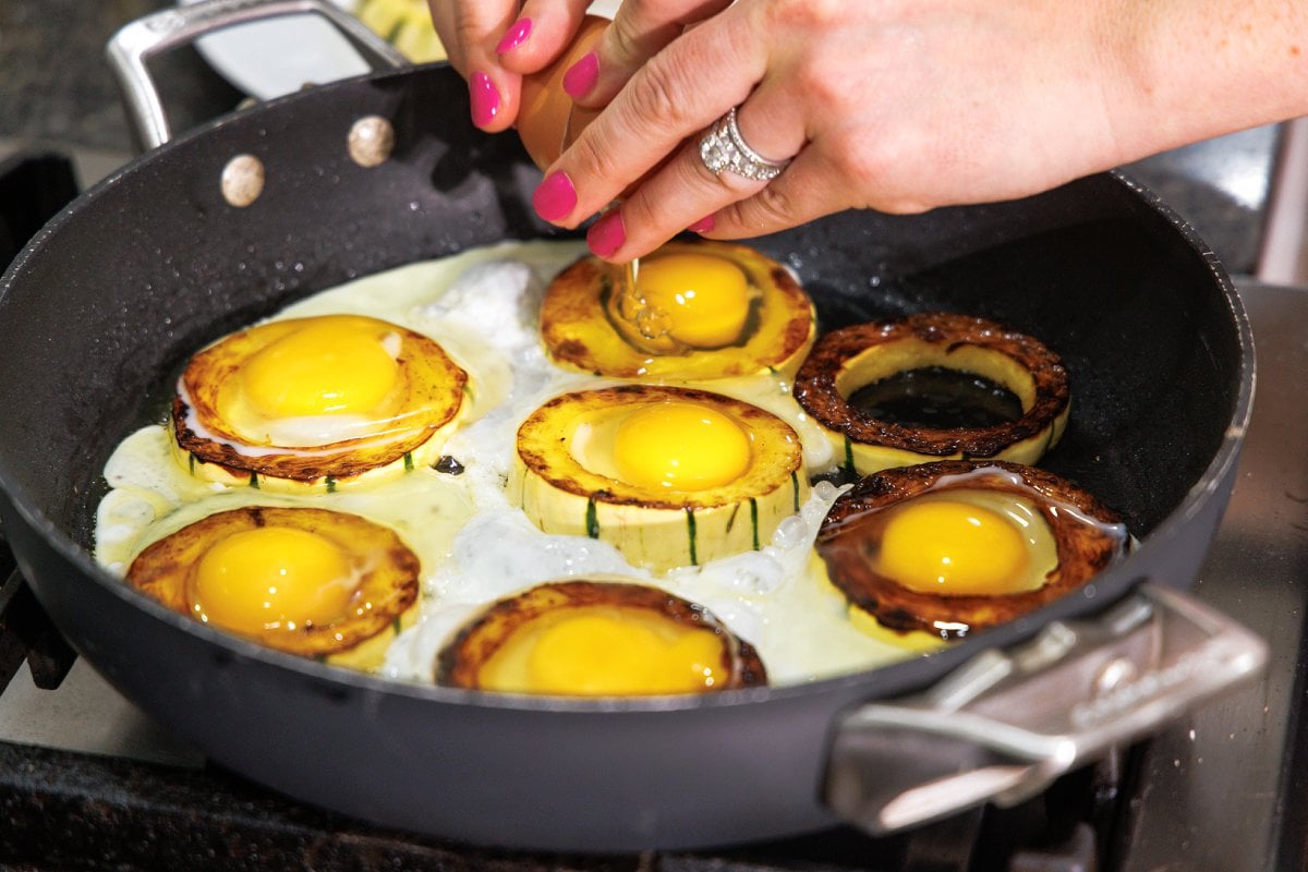 Cracking eggs into the center of delicata squash rings in skillet.