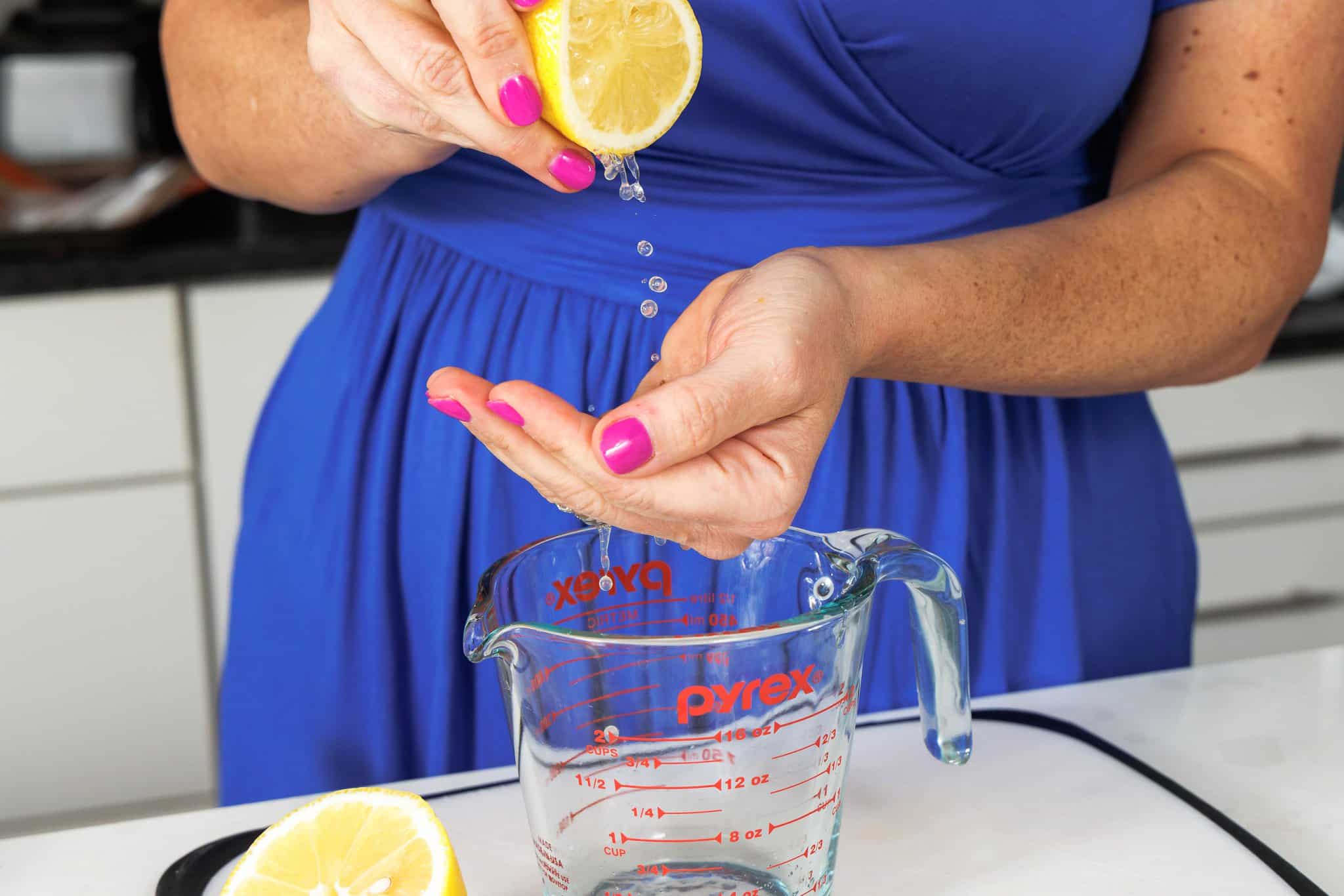 Juicing a lemon cut in half by hand and catching any seeds with the other hand.