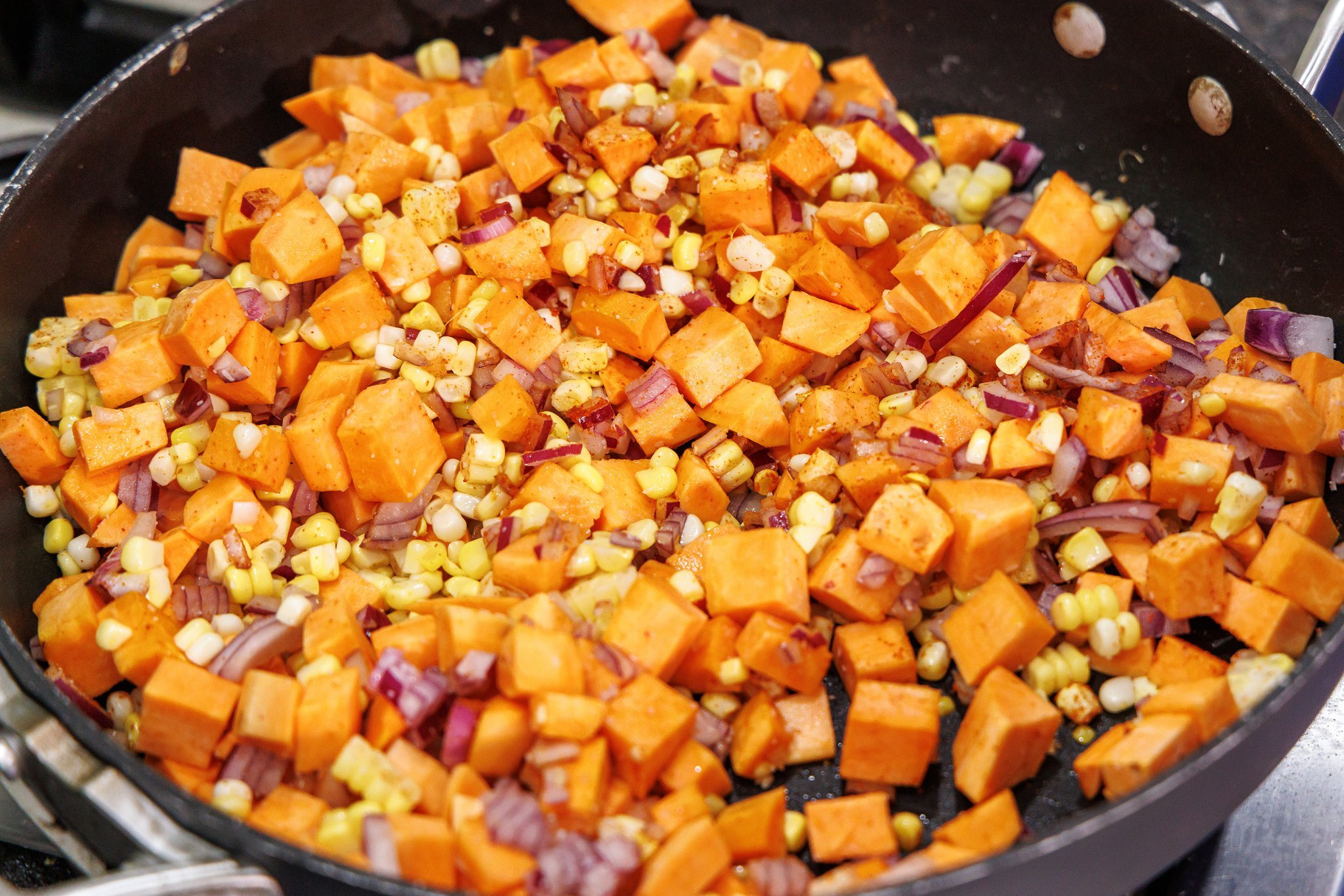 Cooking sweet potato succotash in skillet.