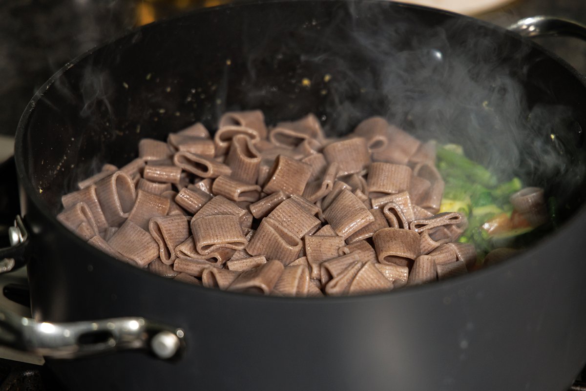 Adding cooked pasta to pot with cooked veggies.