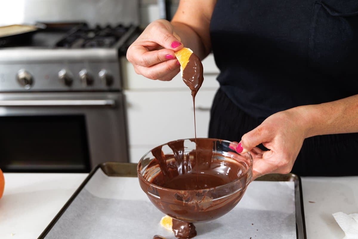 Dipping half of a clementine wedge into melted chocolate.