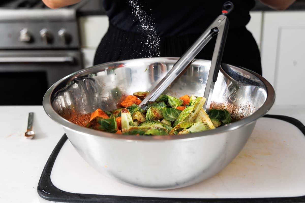 Sprinkling salt onto chopped veggies in a large metal bowl.