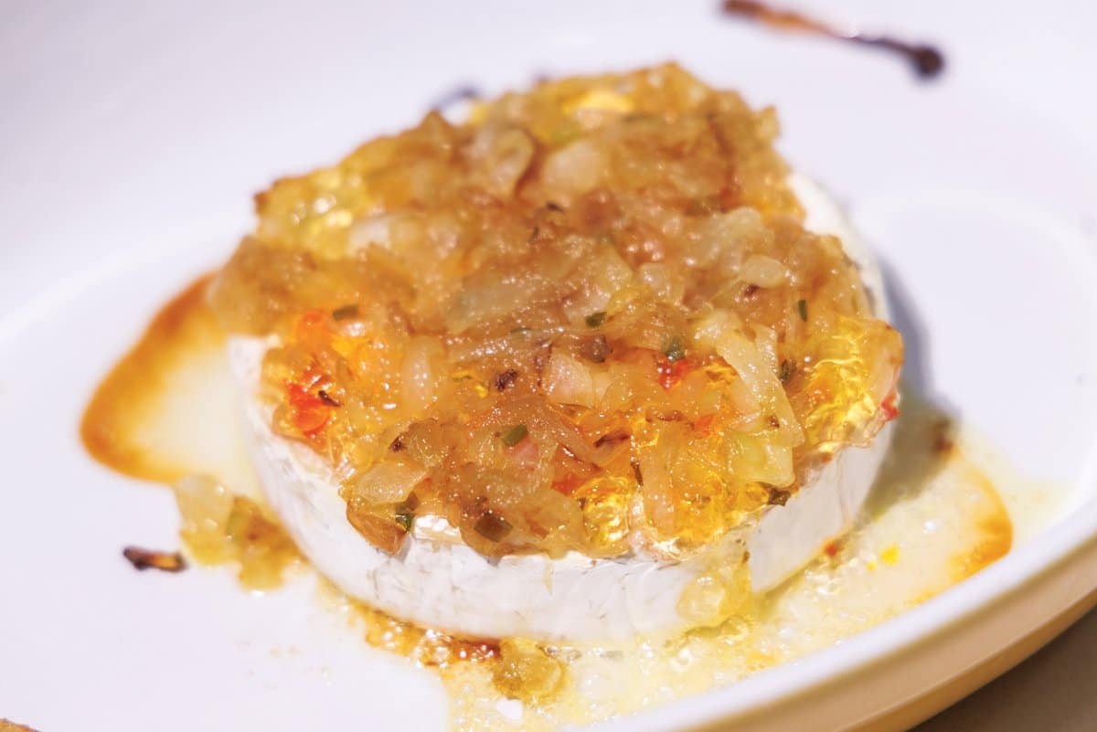 Baked brie with caramelized onions and pepper jelly in a baking dish out of the oven.