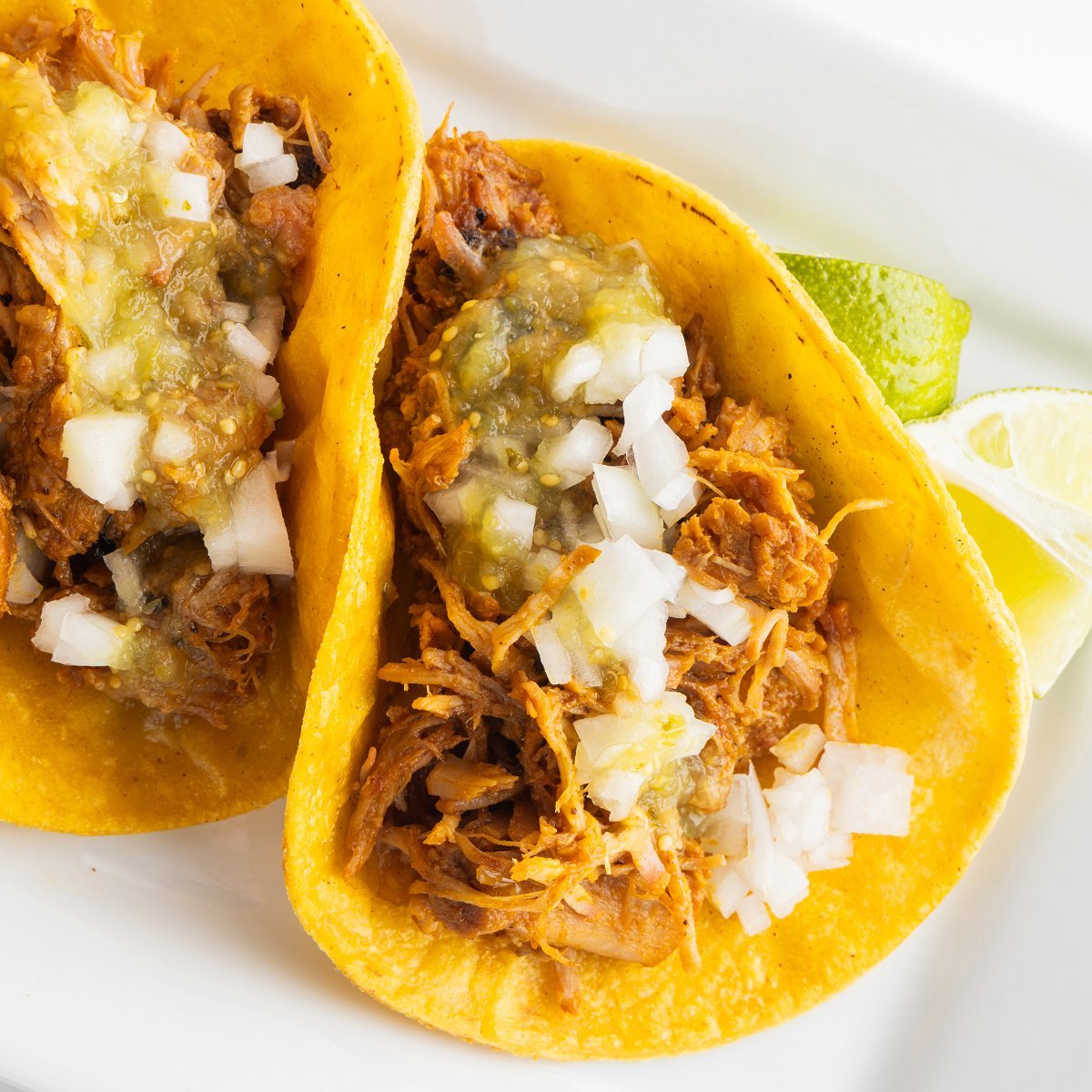 Slow cooker tacos al pastor topped with green salsa and white onion.