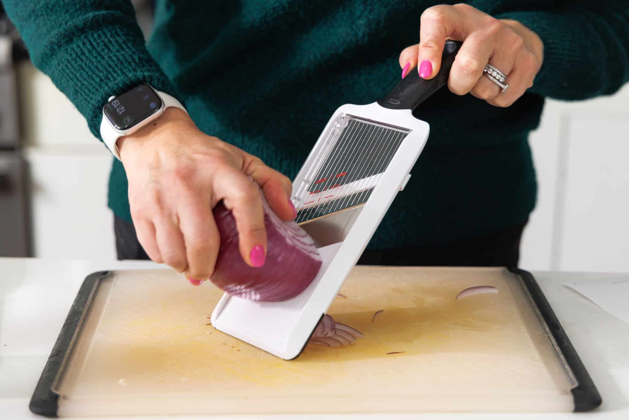 Using a mandoline to thinly slice red onion.