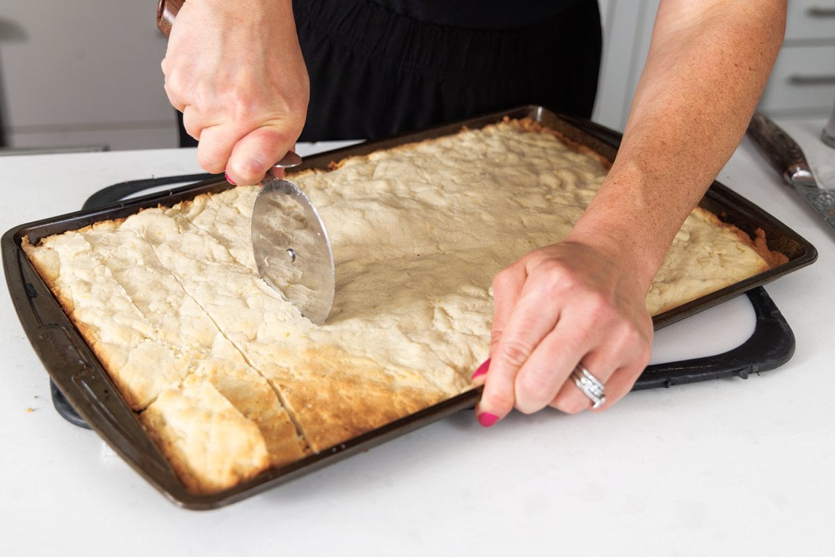 Using pizza cutter to cut shortbread cookies into bars.