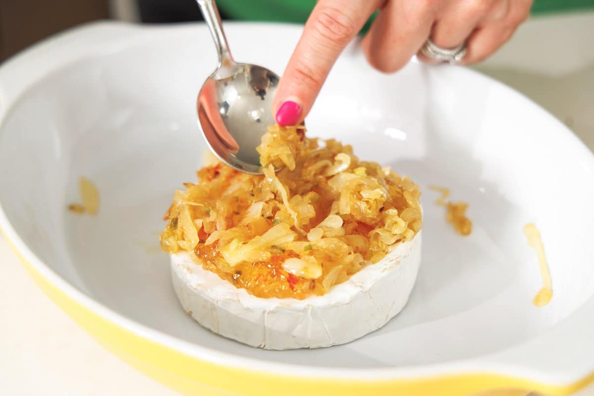 Spooning caramelized onions on top of small wheel of brie.