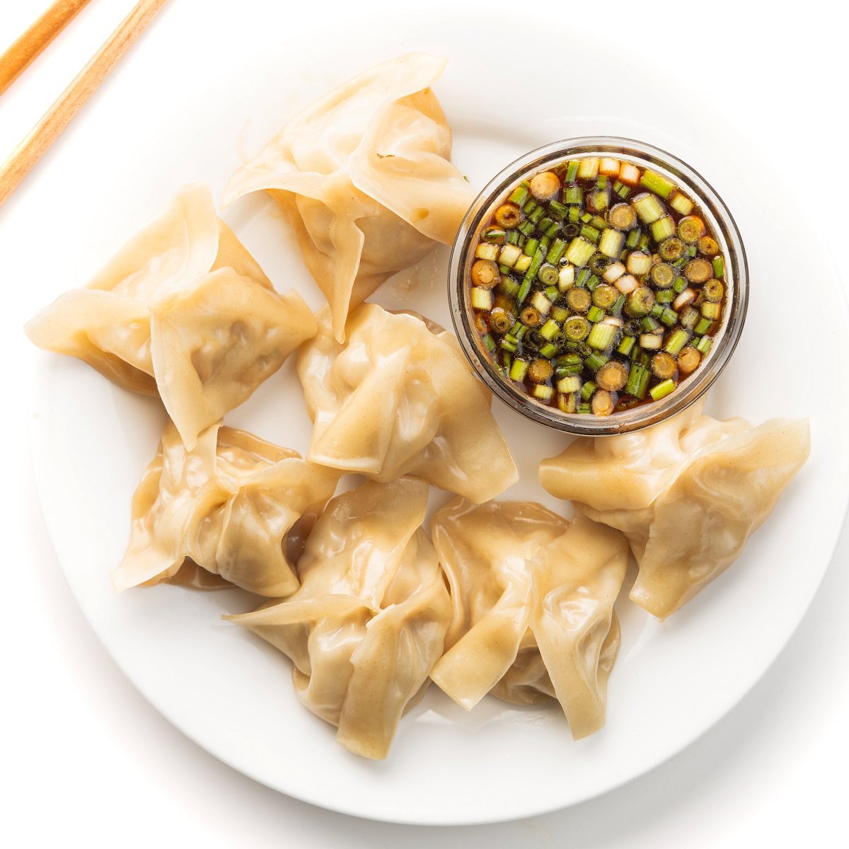 Steamed pork dumplings on a plate with a small bowl of dipping sauce.
