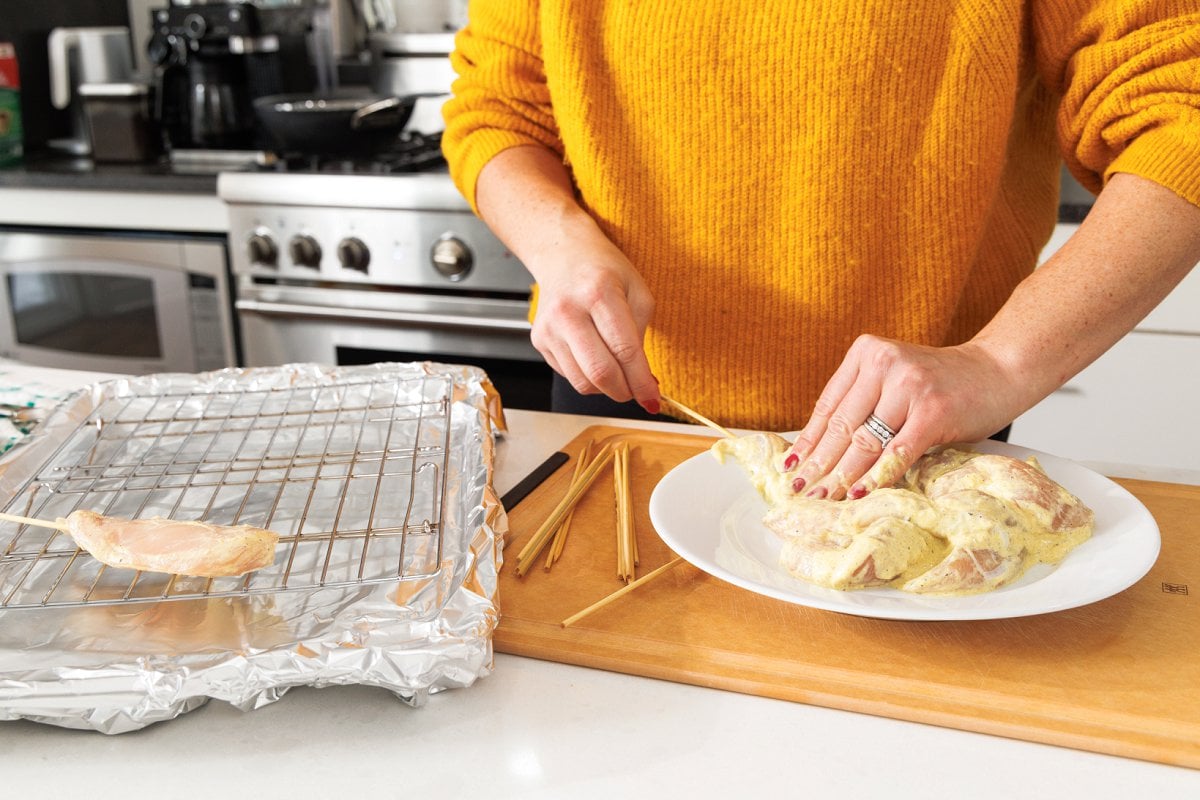 Taking skewered chicken and laying it on a prepared baking sheet.