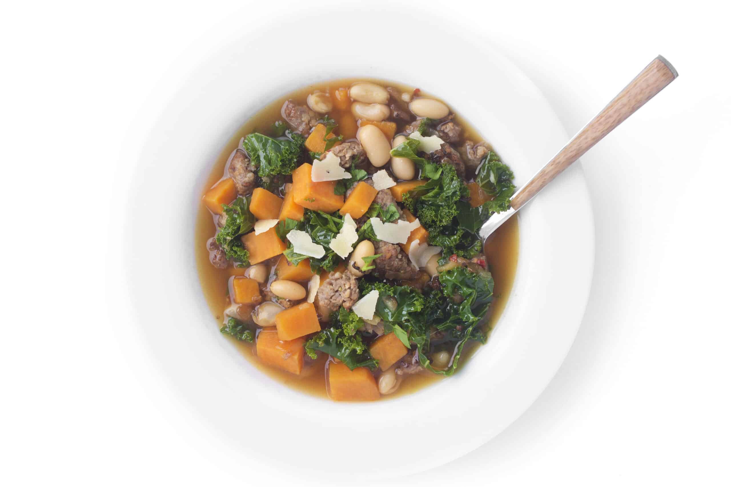 Top down view of a bowl of sausage, bean, and sweet potato soup topped with shaved parmesan cheese.