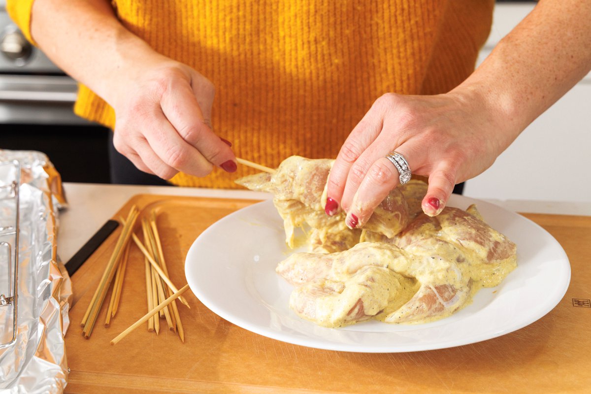 Liz pushing wooden skewer through marinated chicken tenderloin.